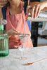a woman pouring a martini from a cocktail tin into a stemmed glass